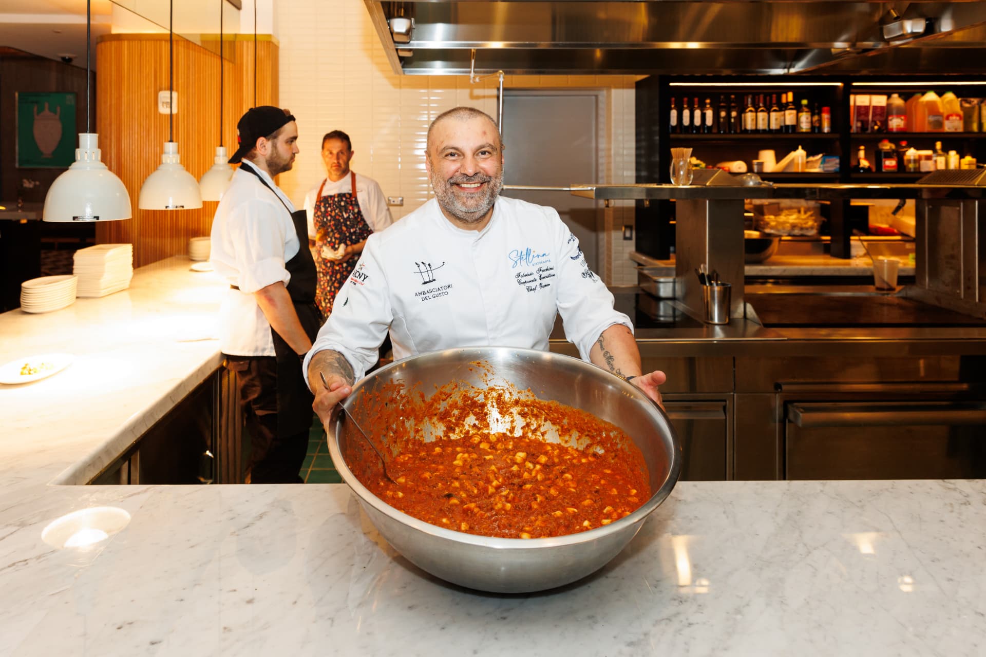 Chef presenting a large batch of freshly made Italian sauce at a live station