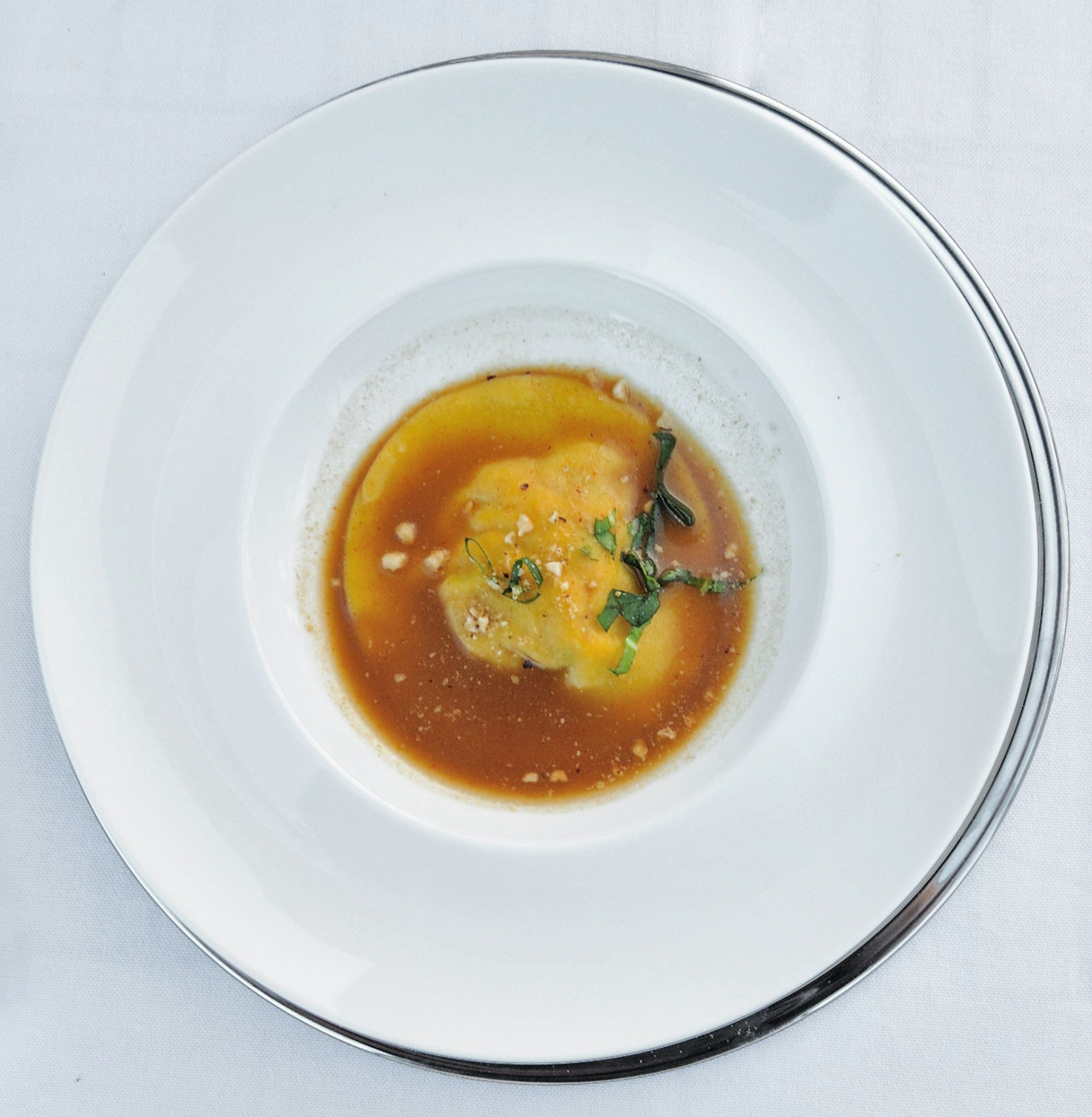 Ravioli in herb broth with crumbs on a large white plate