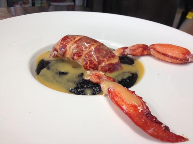 Lobster dish with dark ravioli and orange garnish on a white plate