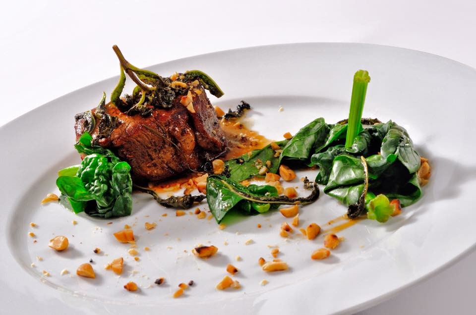 Roasted meat with greens, nuts and sauce on a white plate