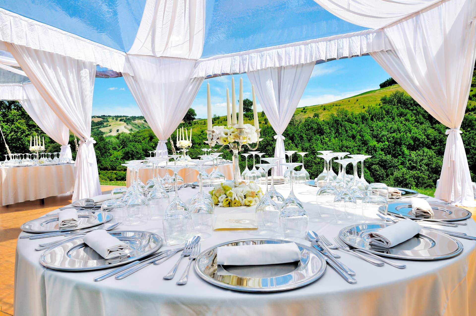 Tented wedding reception table with silver chargers, candelabra and white florals