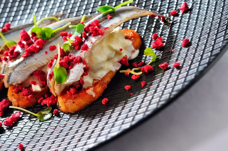 Fish and creamy crostini with red garnishes on a black plate