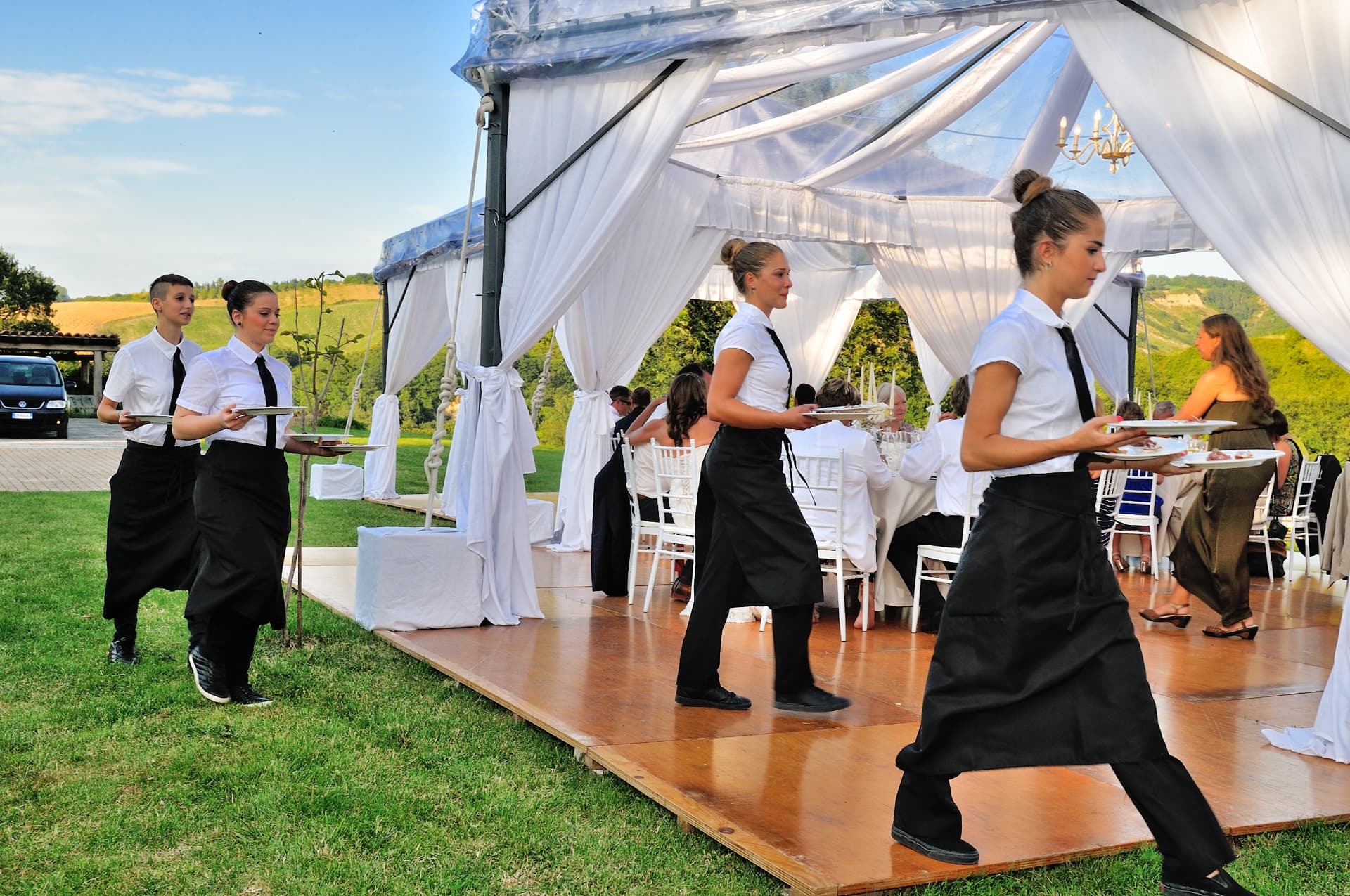 Waitstaff serving plated courses at an outdoor tented wedding reception